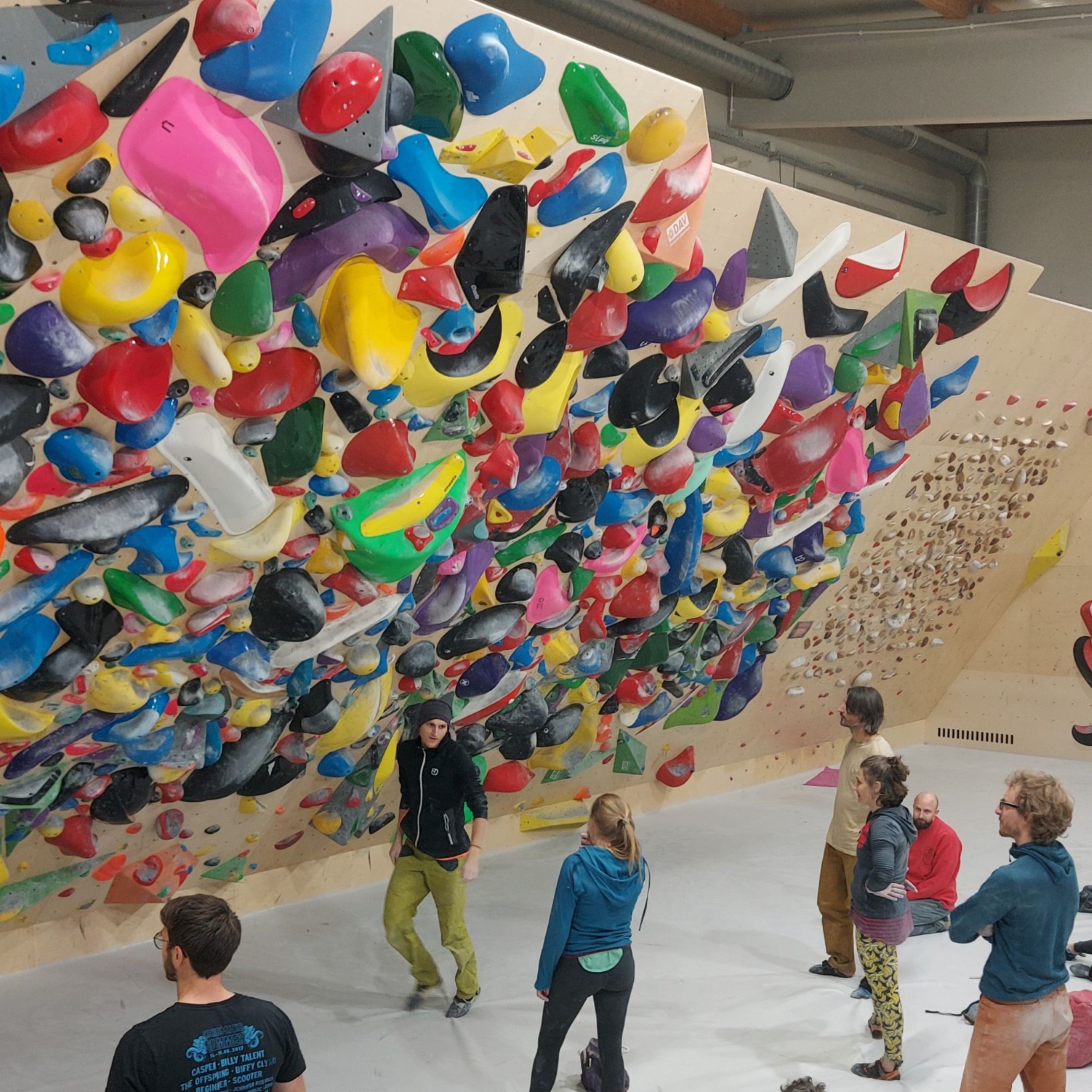 junge Menschen des Bayernkaders, die einen Boulder an der bunten Spraywall definieren